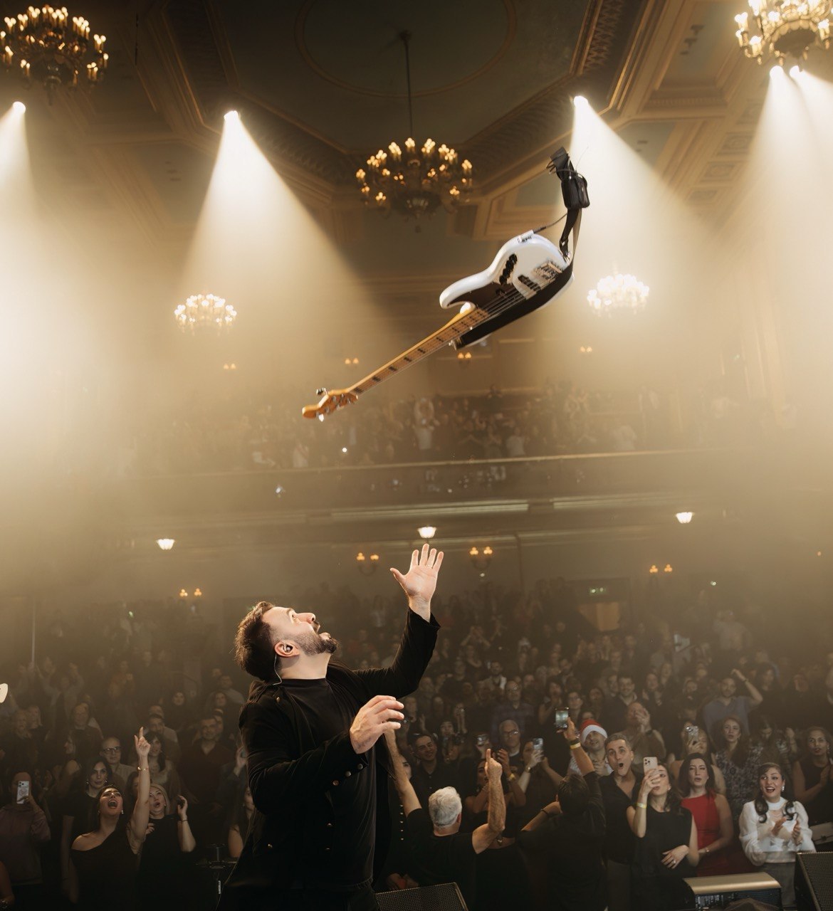 Ali Sanaei performing on stage, with his bass guitar in the air